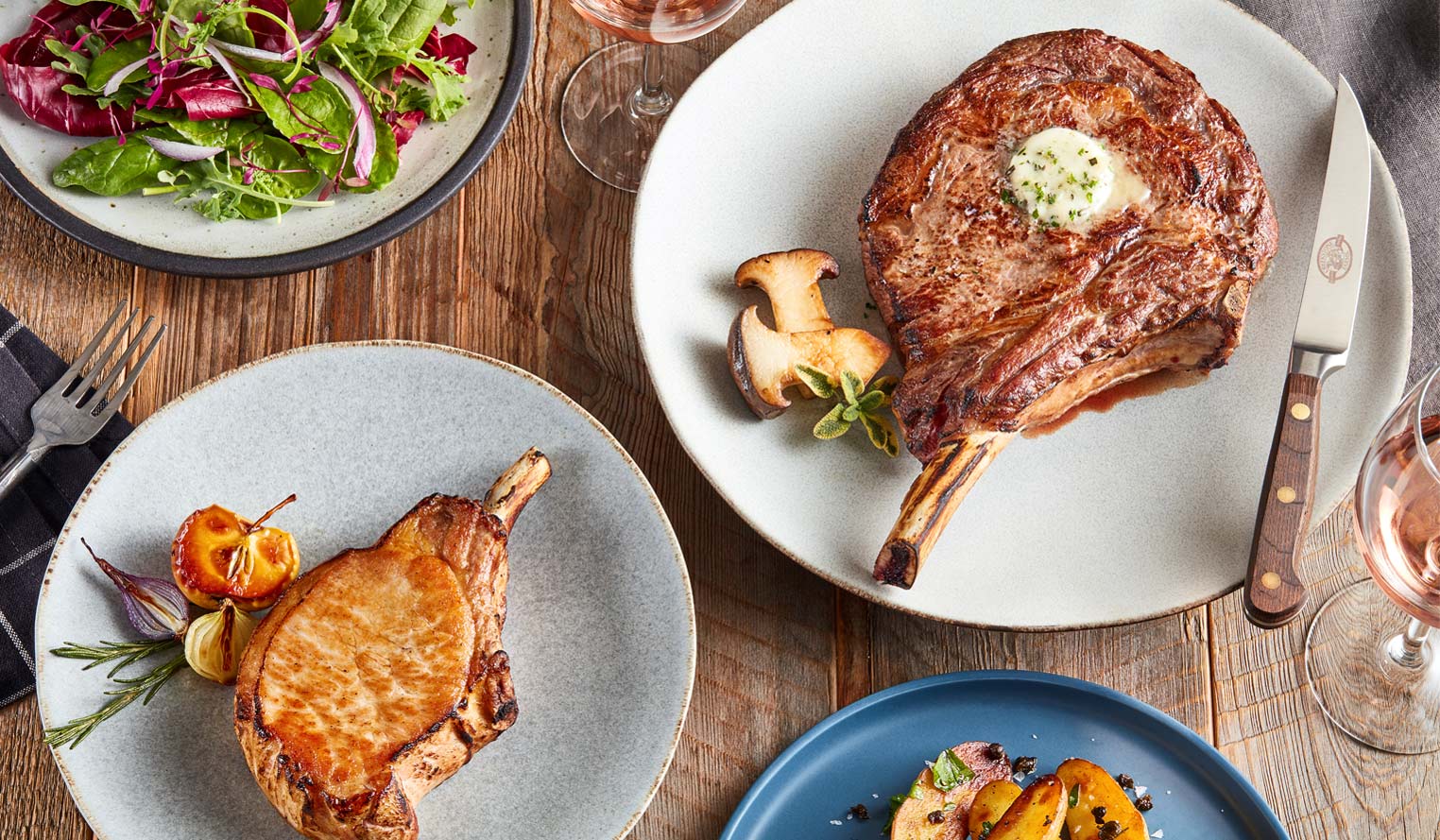 Table setting with a salad, ribeye steak with butter and a knife, and a glass of wine