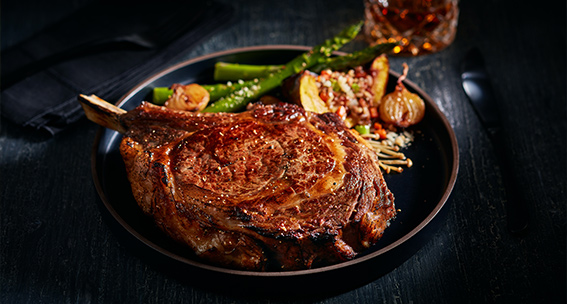 Shiny and juicy ribeye steak plated with fresh asparagus and other vegetables