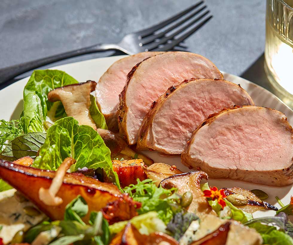 Pork tenderloin slices served with leafy greens and mushrooms