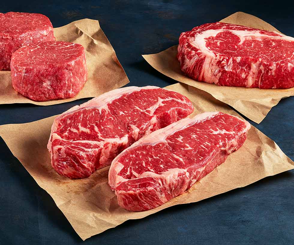 Variety of raw steaks including filet mignon and New York strip laid on butcher paper