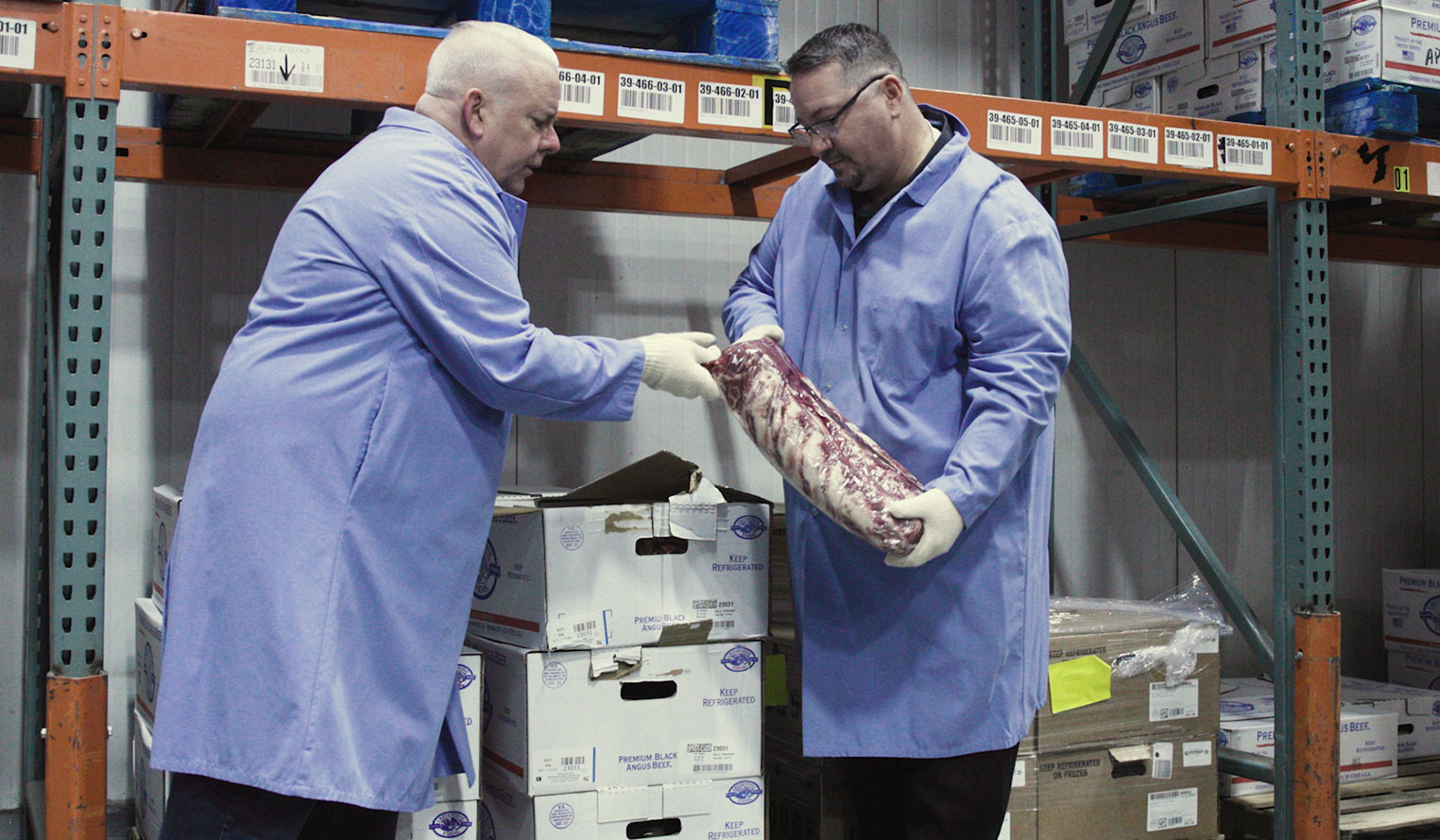 Two men in personal protective equipment jackets and gloves handling packaged meat from delivery boxes