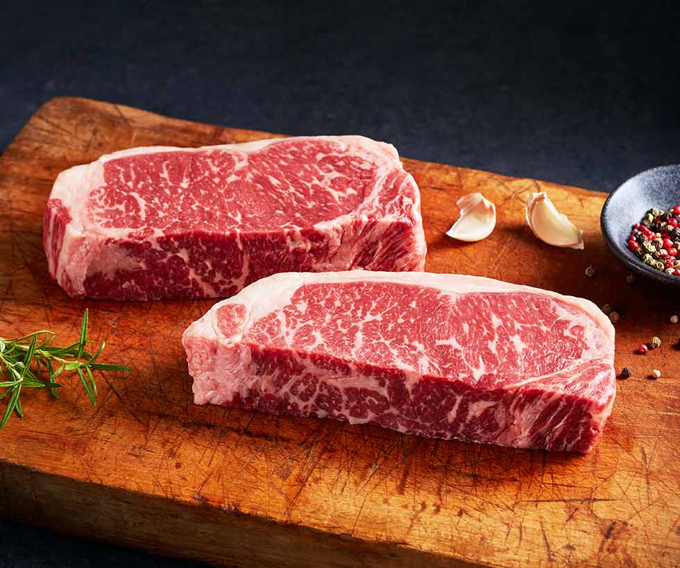 Two raw New York strip steaks on a wooden cutting board