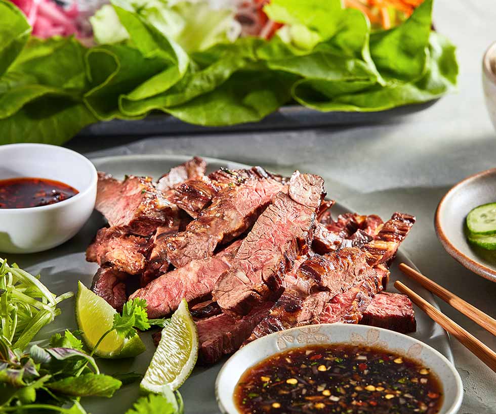 Sliced skirt steak served with a drizzle sauce and leafy greens