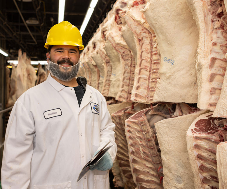 Creekstone Farms Processor standing beside hanging sides of beef